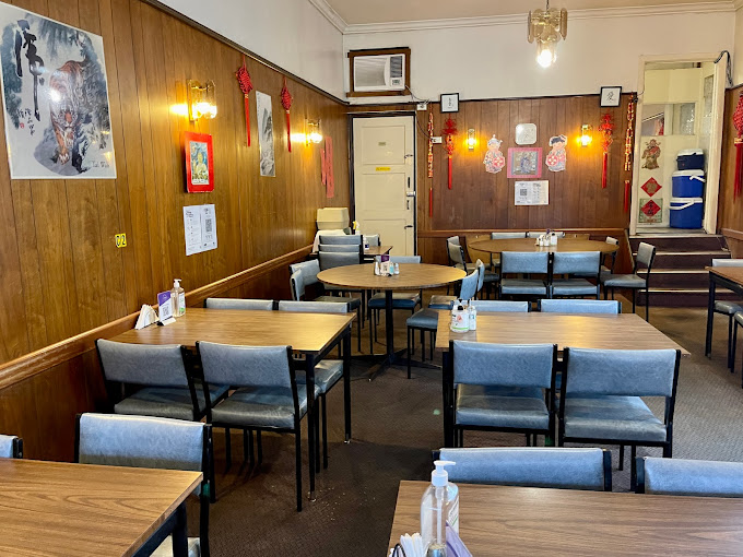 Inside Tai Wah restaurant, with simple wooden wall panels, red Chinese decorations, and blue-grey chairs around square and round tables. The unchanged old-school décor adds to the nostalgic feel, making it a classic spot to enjoy dim sims.